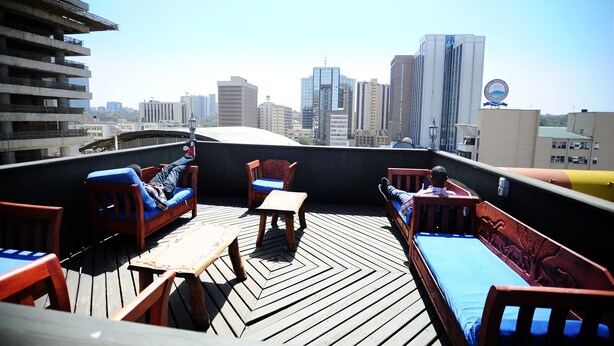 Terraza en la azotea con muebles de madera, vistas del horizonte urbano y un edificio con un logotipo distintivo.