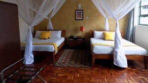 Habitación de hotel con dos camas, cada una con dosel, suelo de madera, alfombra estampada y mesita de noche con lámpara.