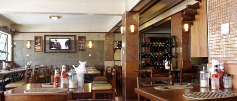 L’intérieur d’un restaurant avec des tables et des chaises en bois, un écran de télévision et un meuble à vin.