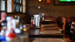 Zona de bar con mostrador de madera, un atril para el menú y una pantalla de televisión al fondo.