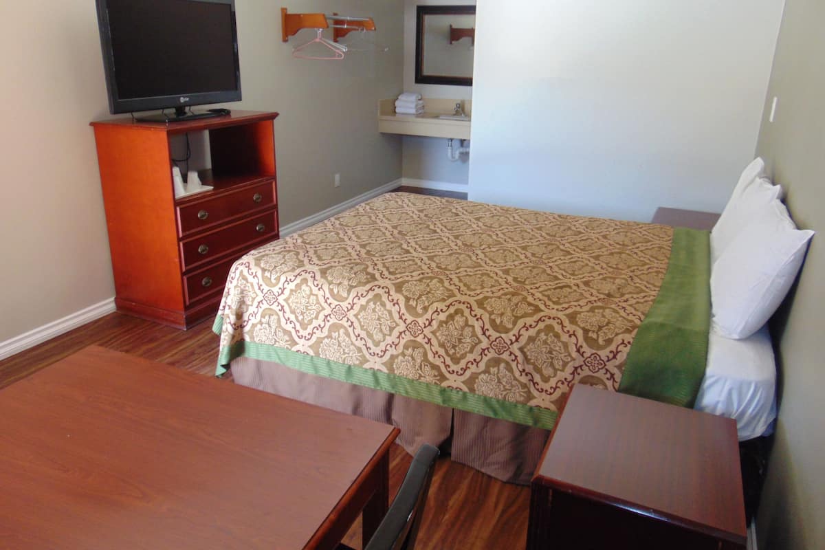 A hotel room with a bed, a TV on a wooden dresser, a bathroom with a sink and mirror, and a small table.
