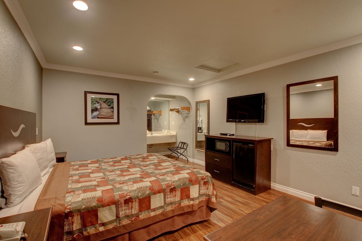 A hotel room with a bed, a desk, a television, a mirror, and a bathroom visible through an archway.