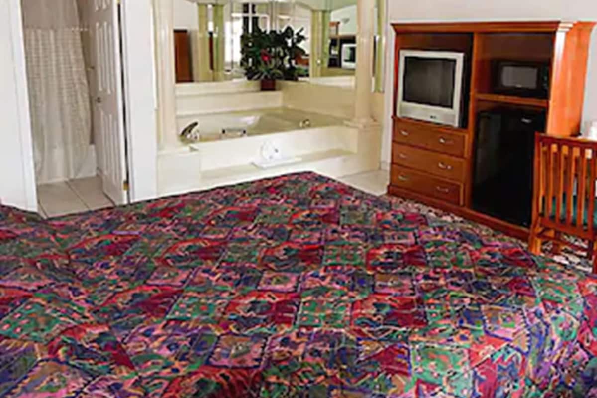 A bedroom with a bed, a dresser, a TV, and a bathroom visible through an open door.