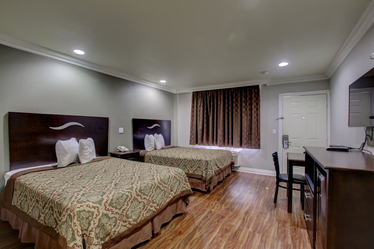 A hotel room with two beds, a desk, a chair, and a door.