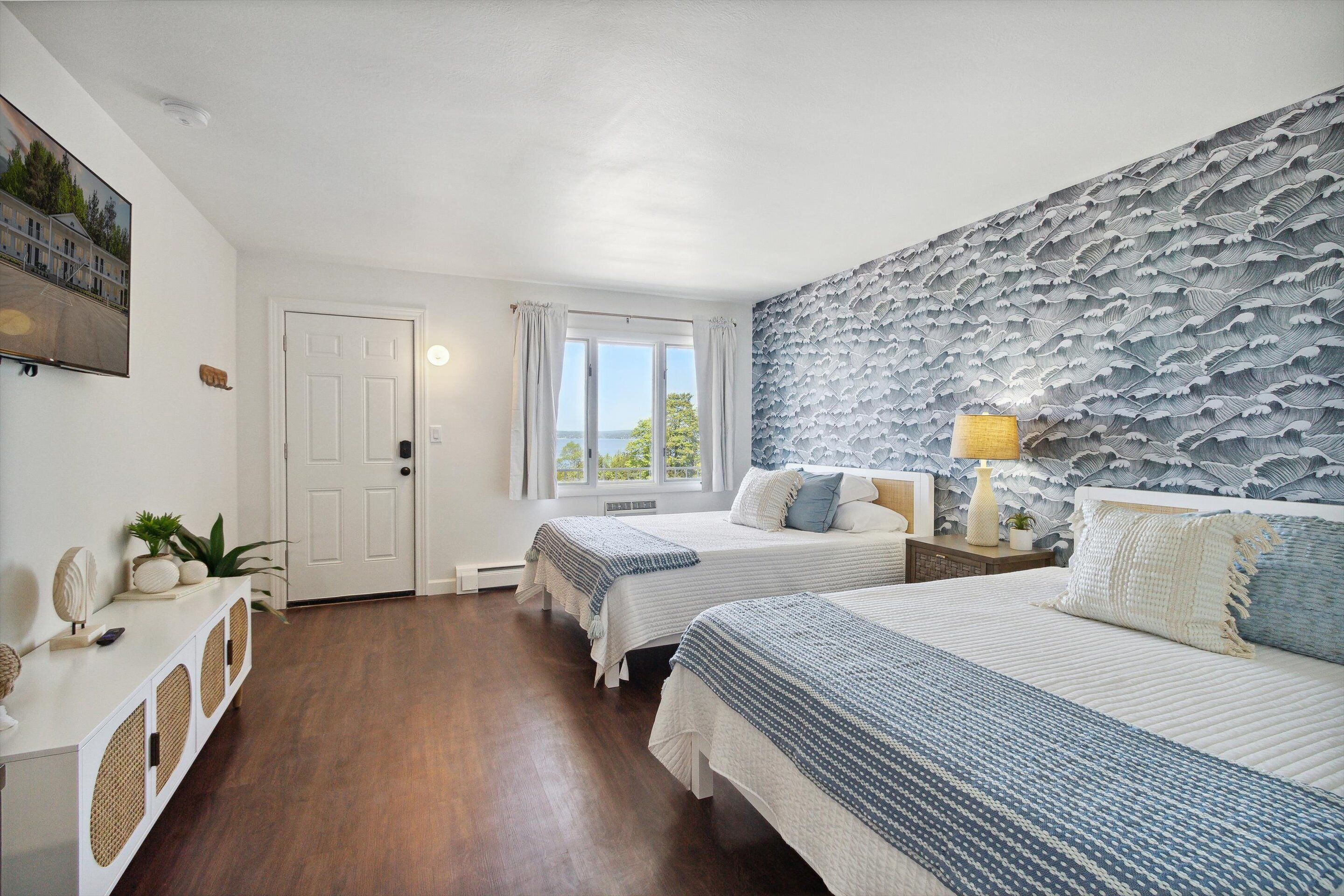 A bedroom with two beds, a large window, and a decorative wall.