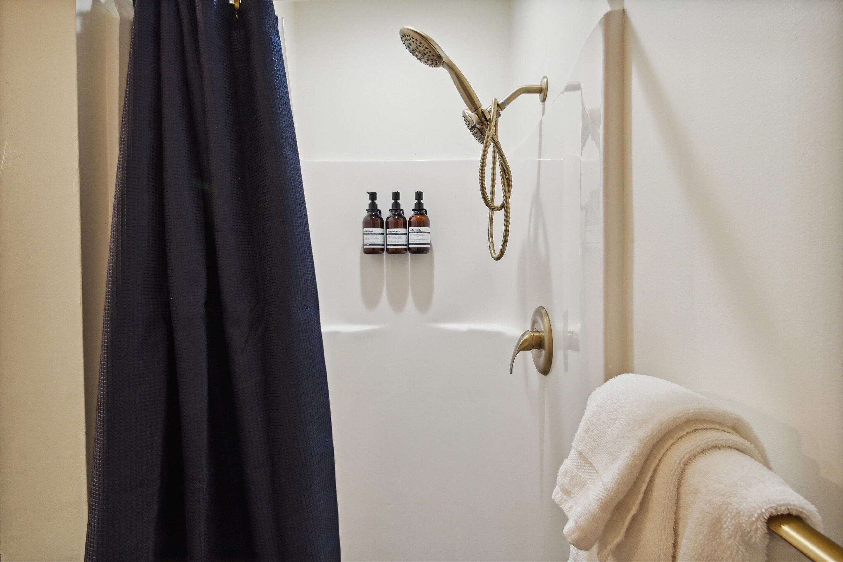 Un baño con ducha, un perchero y tres botellas de champú.