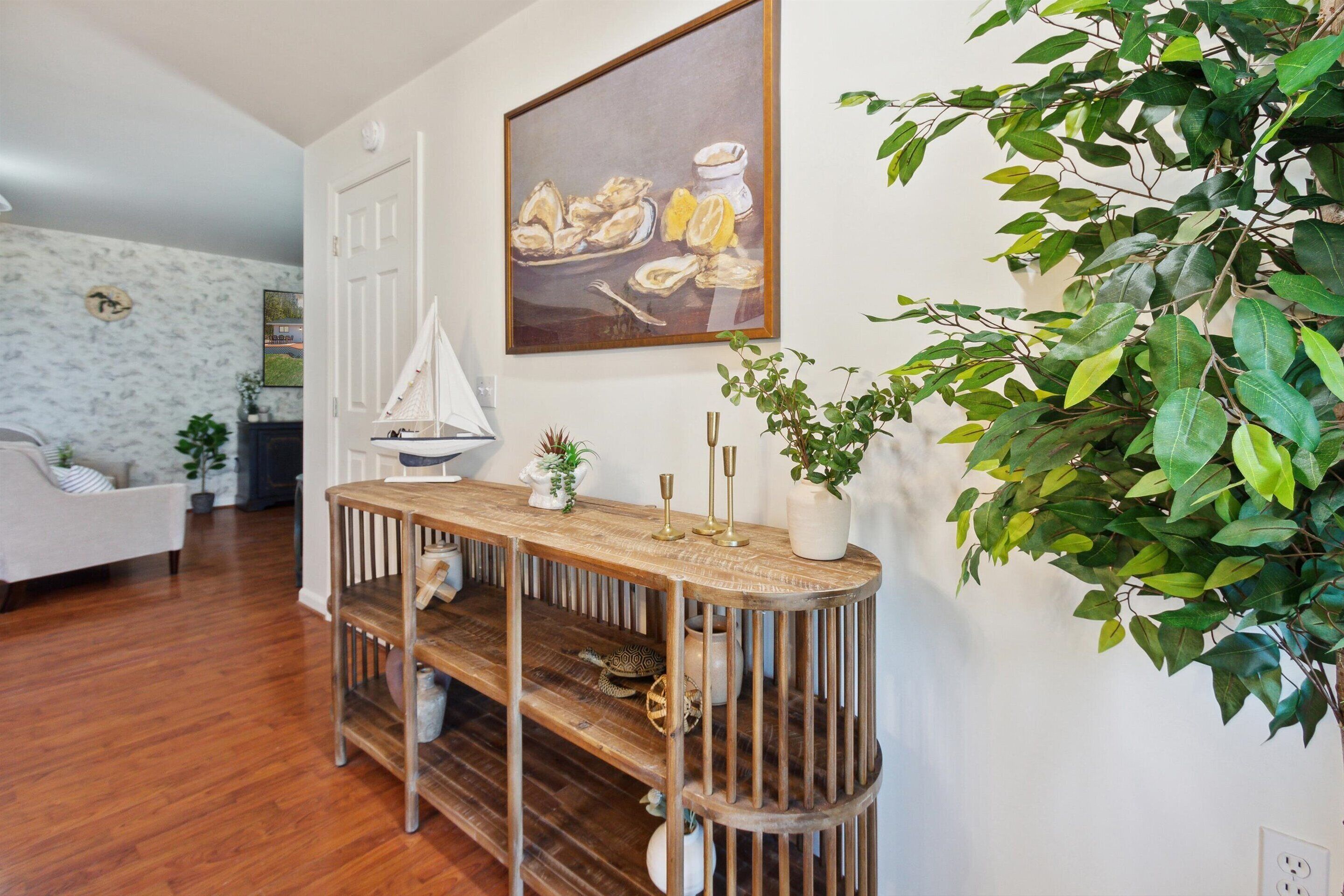 A wooden console table with decorative items and a potted plant, a white sailboat model, and a framed painting on the wall.