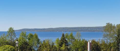 Vue d’une propriété située au bord de l’eau, avec une clôture blanche, des arbres et un ciel bleu dégagé.