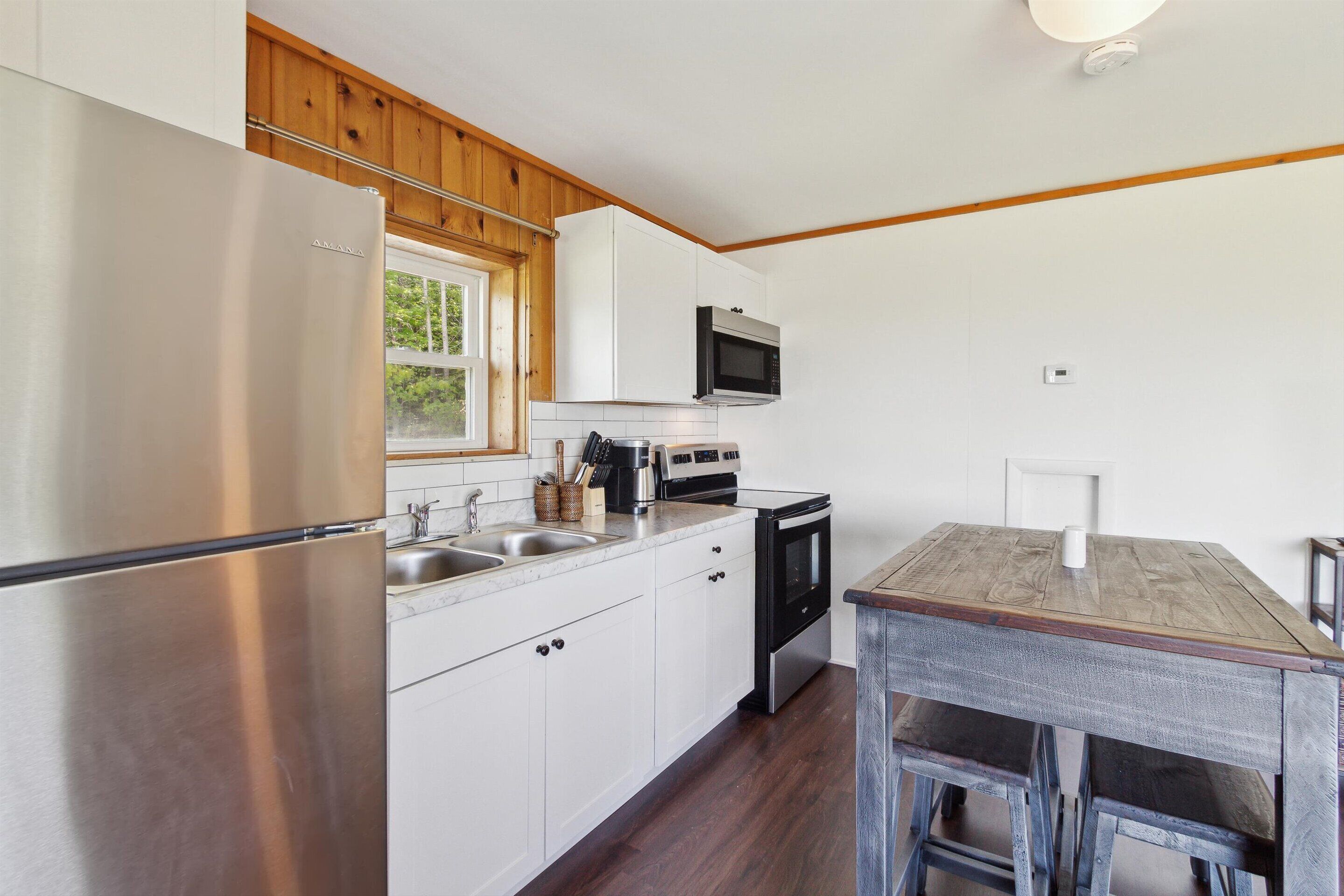 Una cocina compacta con armarios blancos, un refrigerador de acero inoxidable, un microondas y una estufa.
