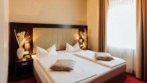 Ein Hotelzimmer mit einem großen Bett, zwei Nachttischen, einem Kopfteil und einem Fenster mit Vorhängen.