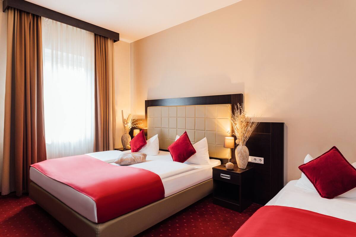 A hotel room with a large bed, two bedside tables, a nightstand, and a window with curtains.