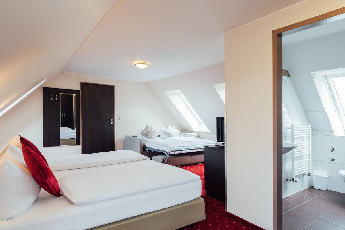 A modern hotel room with a large bed, a desk, and a small seating area. There is a skylight and a view of the outside.