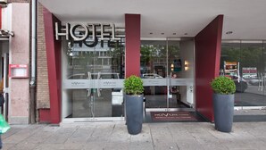 Ein Hotel mit gläserner Fassade, einer roten Säule und zwei Blumentöpfen.