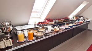 Ein Buffet mit verschiedenen Speisen und Getränken, einer Kaffeemaschine und Blick auf die Stadt durch ein Oberlicht.