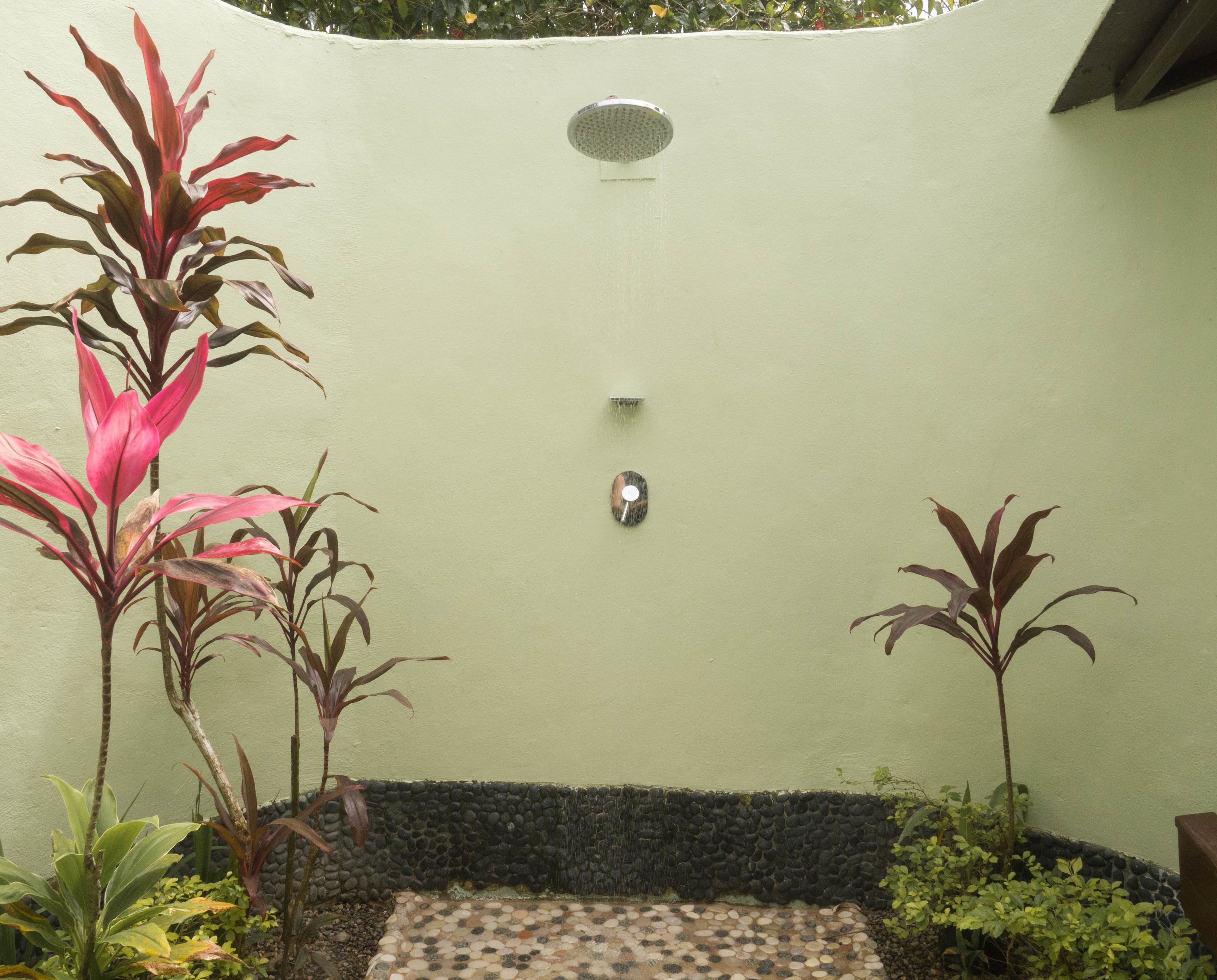 A small, enclosed outdoor shower area with a tiled floor, surrounded by various plants.
