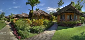 A resort with thatched-roof cottages, a wooden pathway, and lush greenery. - Uprising Beach Resort (Pacific Harbour)