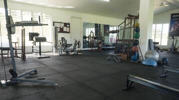 A gym with various exercise equipment, large windows, and a ceiling fan.
