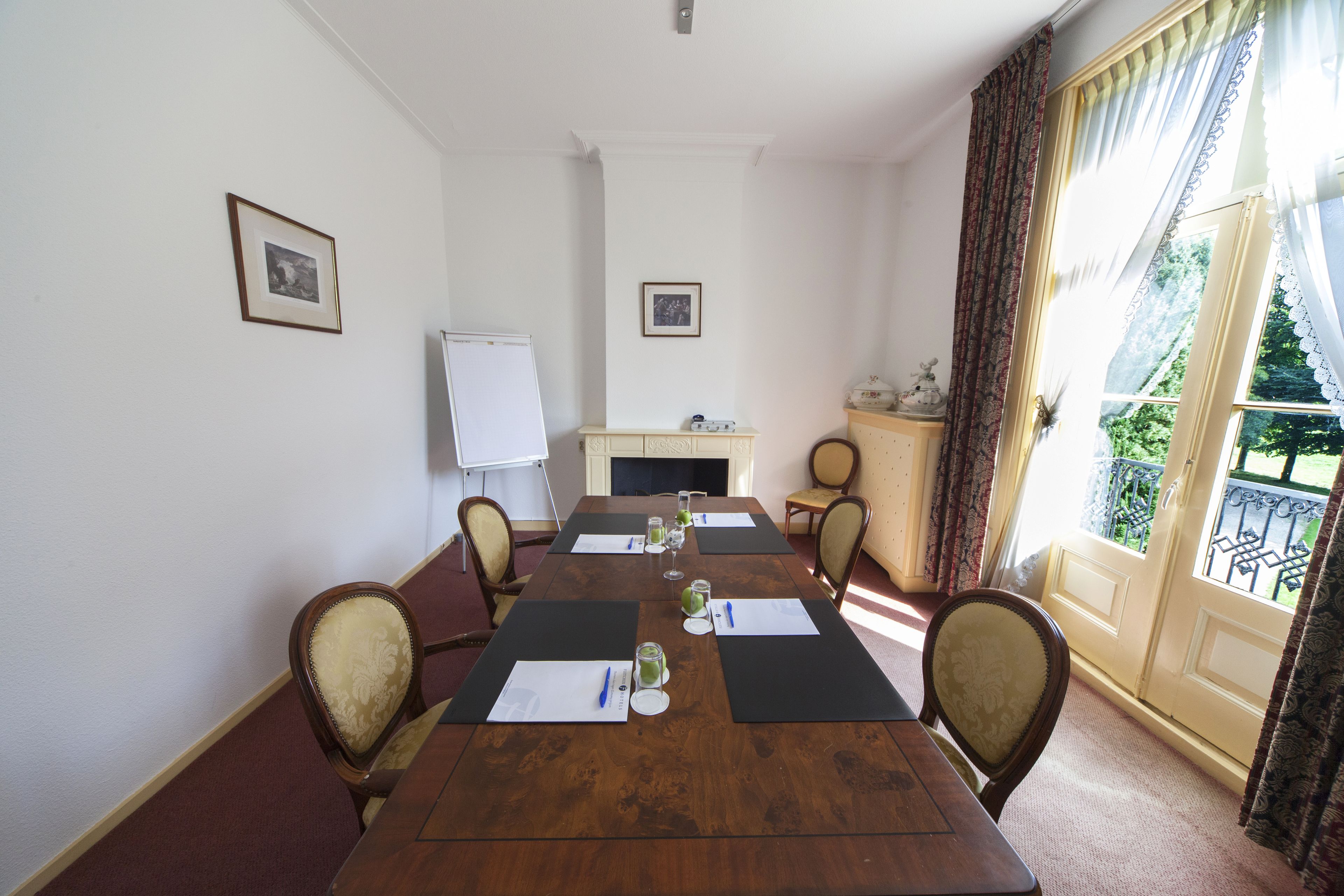 A conference room with a long wooden table, chairs, a whiteboard, and a fireplace.