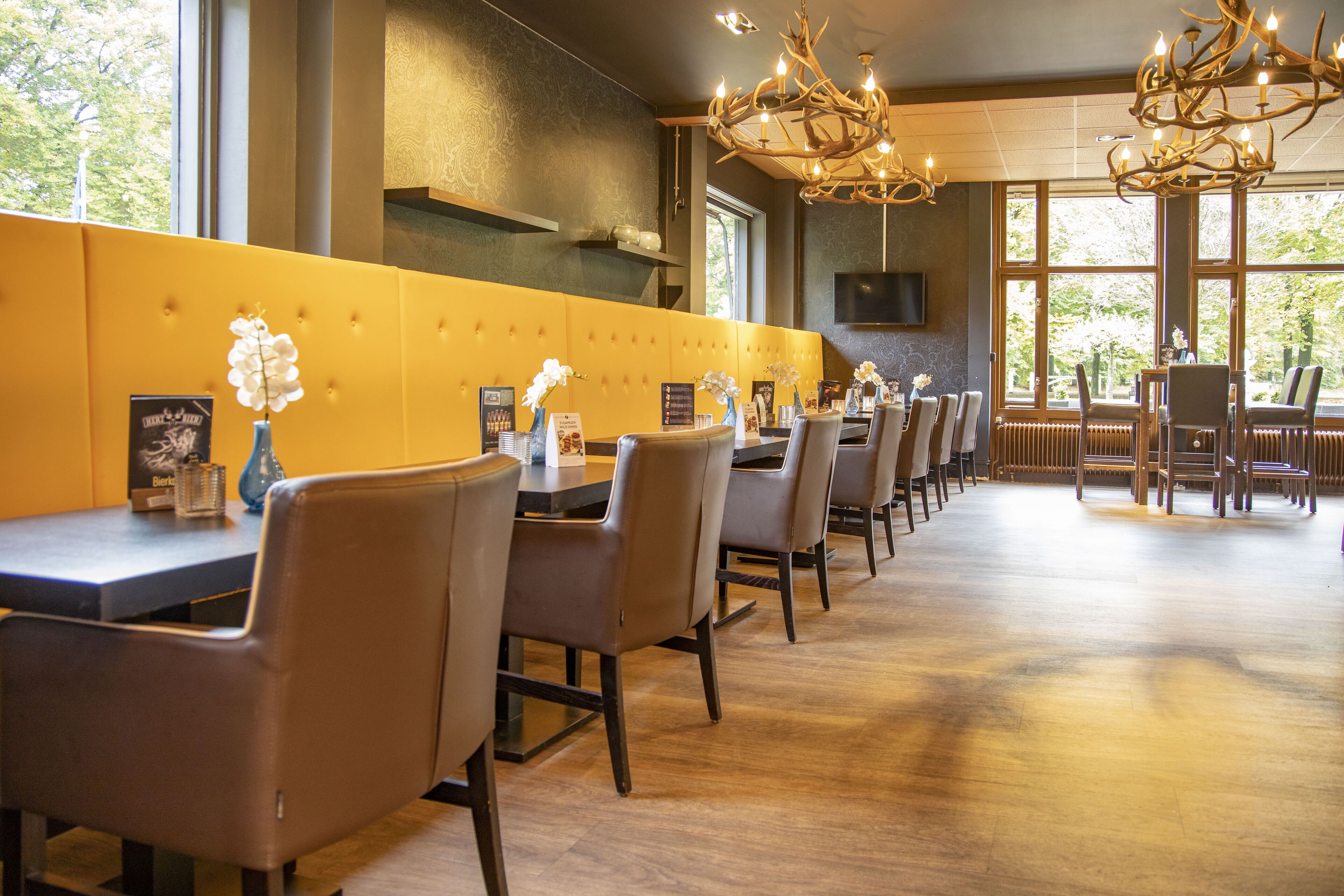 A restaurant with a long counter, multiple tables, and chairs. There are vases with flowers on the tables.