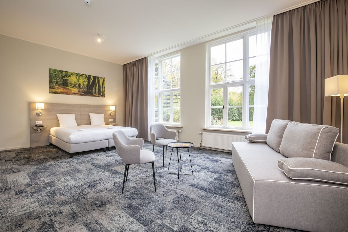 Ein Hotelzimmer mit einem großen Bett, einer Couch, zwei Sesseln, einem kleinen Tisch und einem Bild an der Wand.