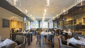 Un restaurant moderne doté de nombreuses tables et chaises, de grands luminaires suspendus et d’un menu écrit à la craie sur le mur.