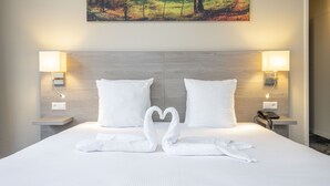 Une chambre d’hôtel avec un lit bien fait, deux oreillers, deux lampes de chevet et un tableau représentant un paysage accroché au mur.