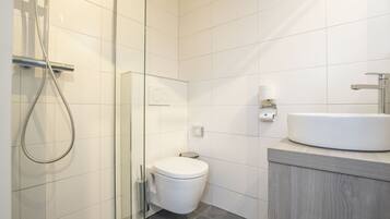 Een moderne badkamer met een douchecabine van glas, een wit toilet en een houten wastafelmeubel met een wastafel.