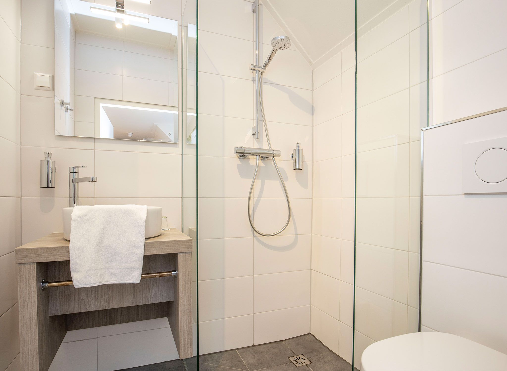 Ein modernes Badezimmer mit einer Duschkabine aus Glas, einem Holzwaschtisch und einer weißen Toilette.