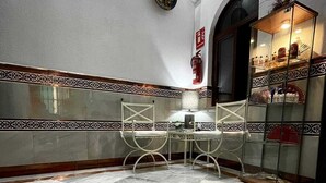 A dining area with a star-patterned floor, white chairs, a glass cabinet with dishes, and a fire extinguisher on the wall. - Hostal Paco's (Seville)