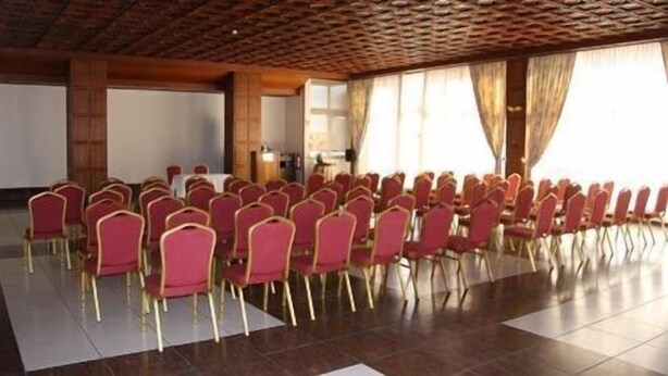 A conference room with rows of red chairs, a whiteboard, and a podium.