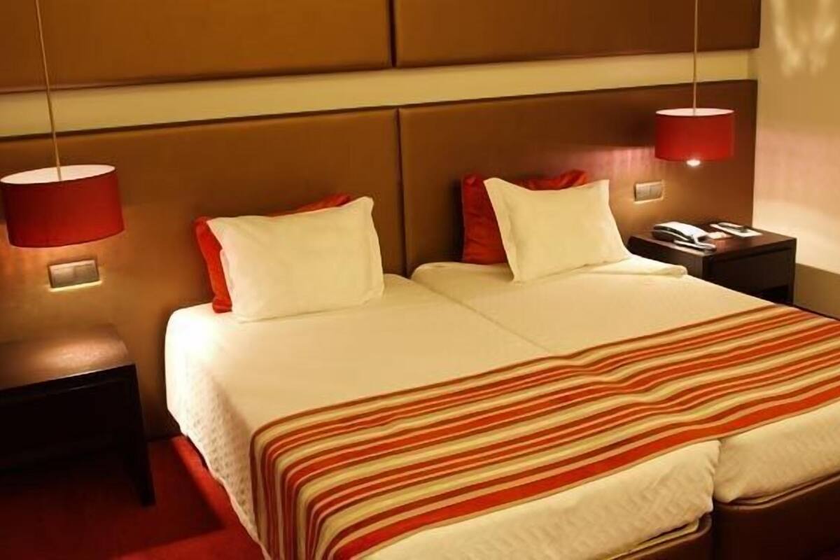 A hotel room with a double bed, two bedside tables, a telephone, and a red lamp on each side.