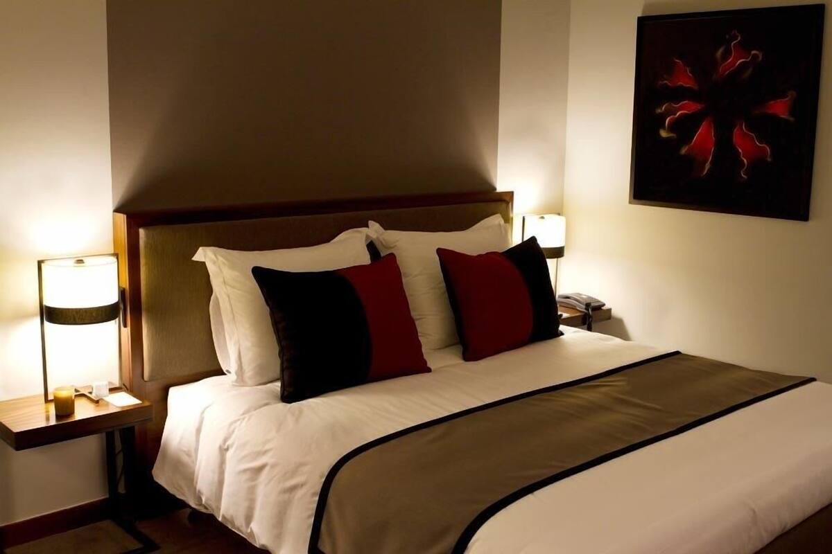 A hotel room with a bed, nightstands, a lamp, and a painting on the wall.