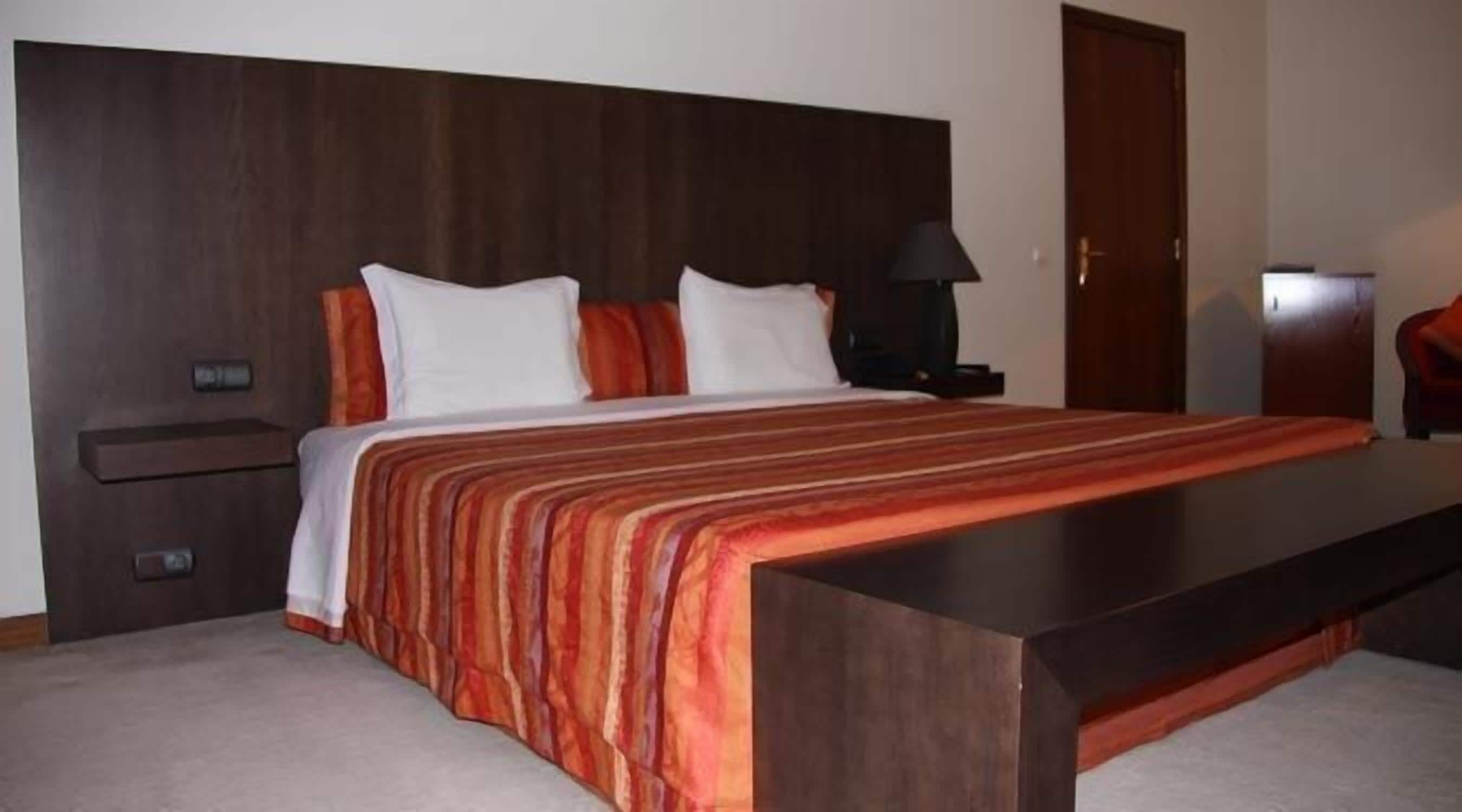 Ein Hotelzimmer mit einem großen Bett, einem Nachttisch, einer Lampe und einem hölzernen Kopfteil.