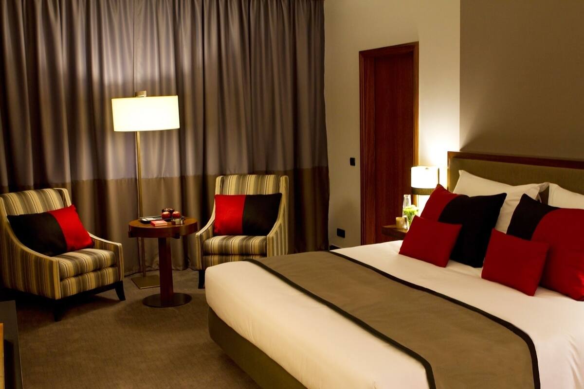 A hotel room with a large bed, two armchairs, a small table, and a lamp.