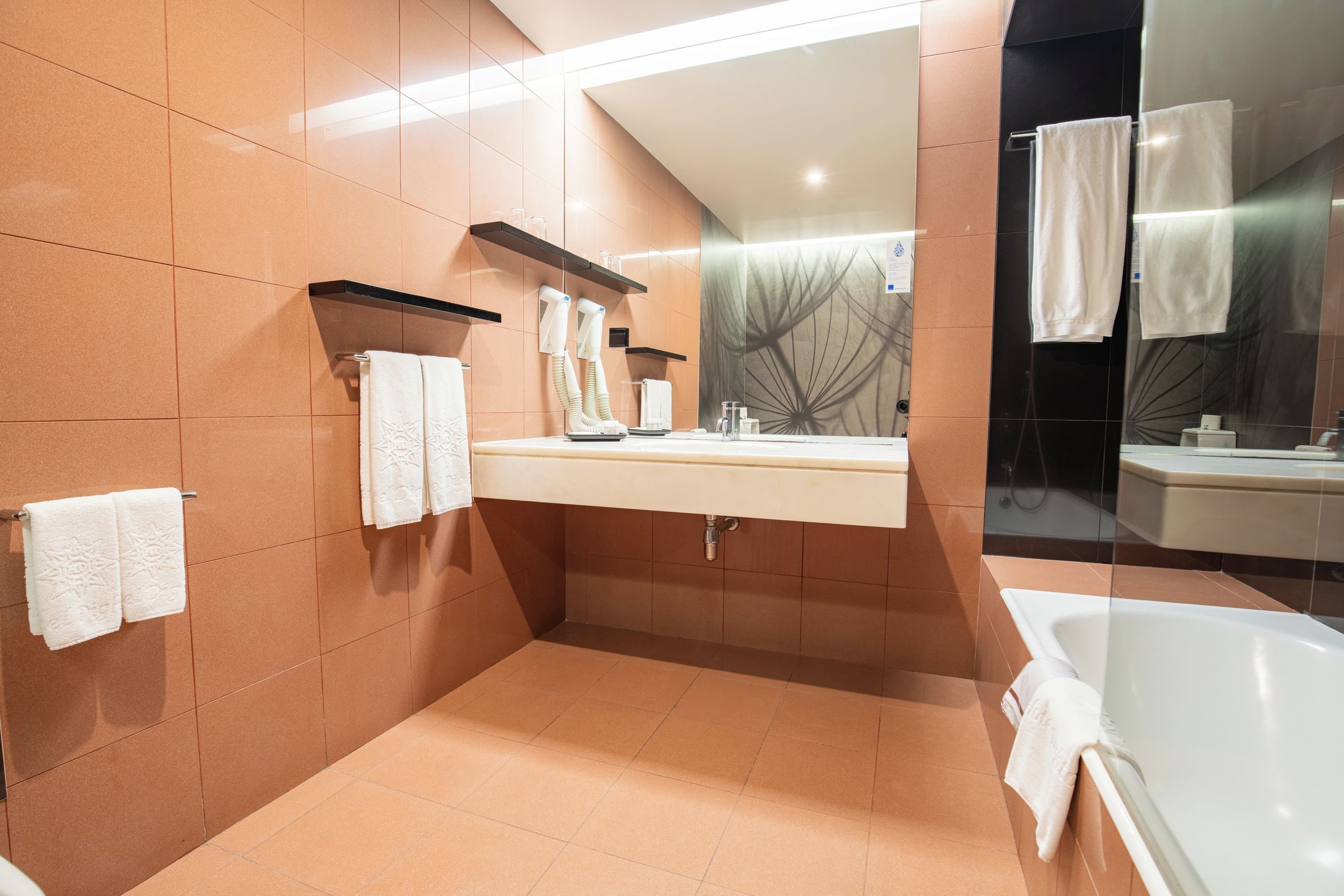 Ein modernes Badezimmer mit einer Badewanne, einem Waschtisch mit Spiegel und Handtuchhaltern.