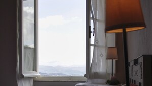 Een slaapkamer met een bed, een raam met gordijnen, een nachtkastje met een lamp en een radiator.