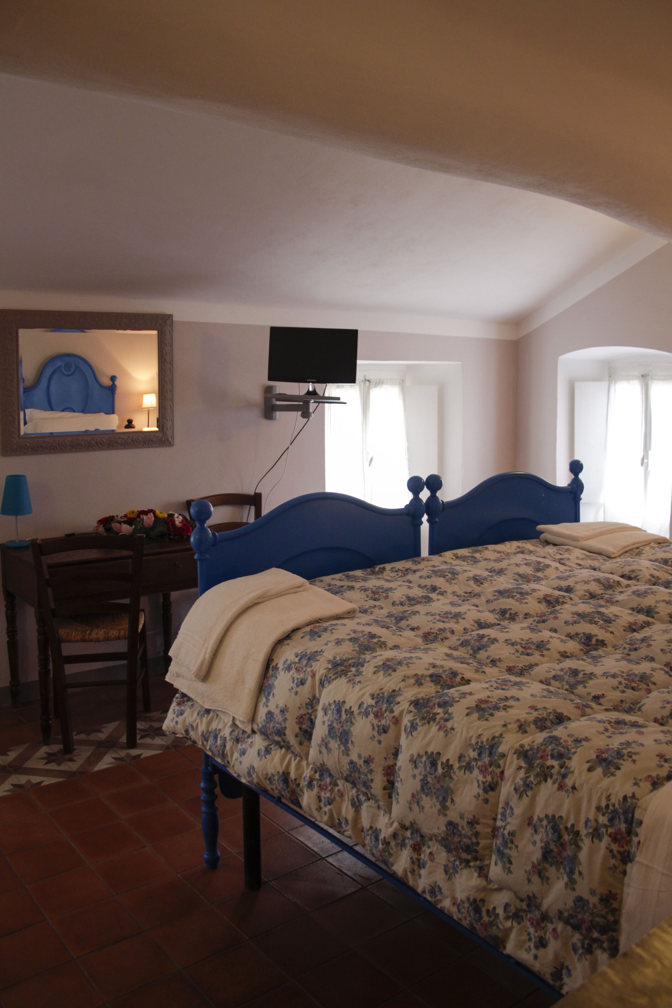 A bedroom with a bed, a desk, a chair, a television mounted on the wall, and a window with curtains.