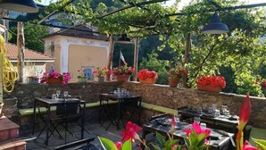 Een terras buiten met stenen muren, tafels en stoelen, omringd door potplanten en bloemen.