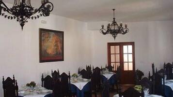 A dining room with multiple tables set for service, a large painting on the wall, and two chandeliers.