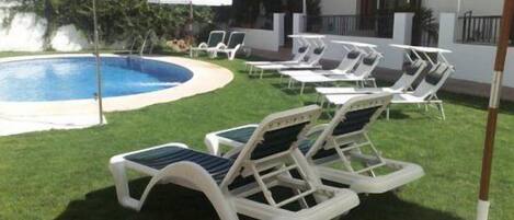 Un área junto a la piscina con sillones de descanso y sombrillas.