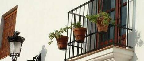 Un edificio con balcón, plantas en macetas y un aplique de pared.