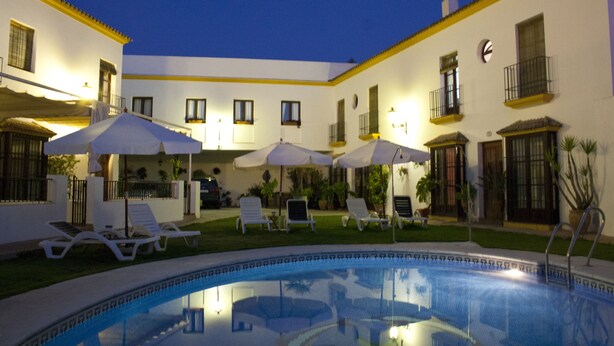 A pool area with lounge chairs and umbrellas, surrounded by a building with balconies and windows.