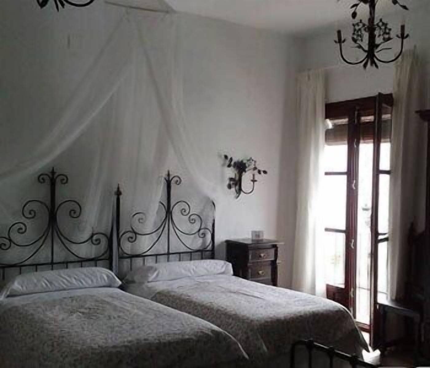 Un dormitorio con dos camas, una araña, una mesita de noche y una ventana con cortinas.