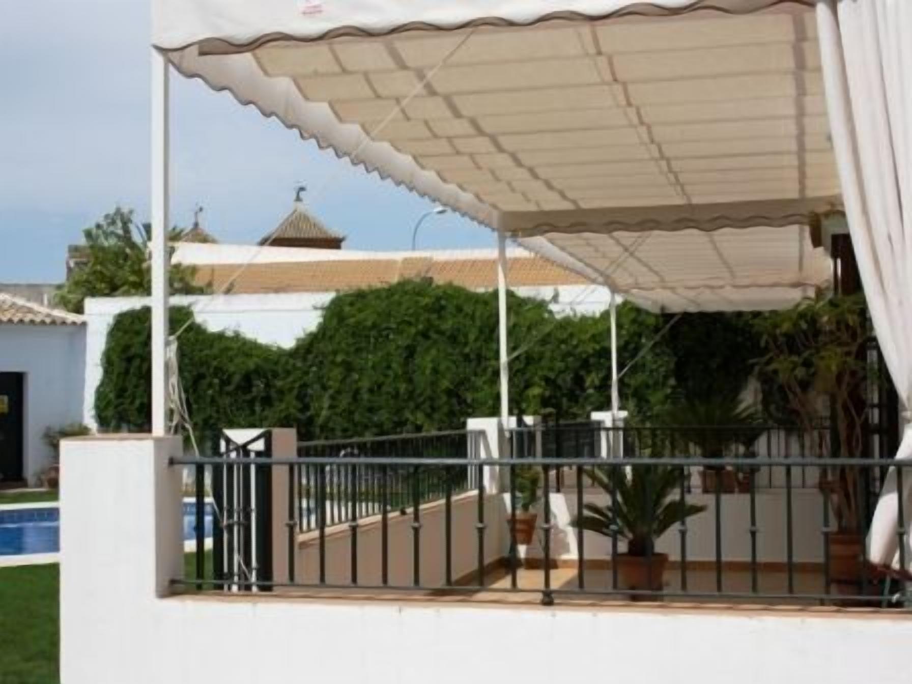 A covered outdoor area with a metal railing, potted plants, and a view of a building with a tiled roof.