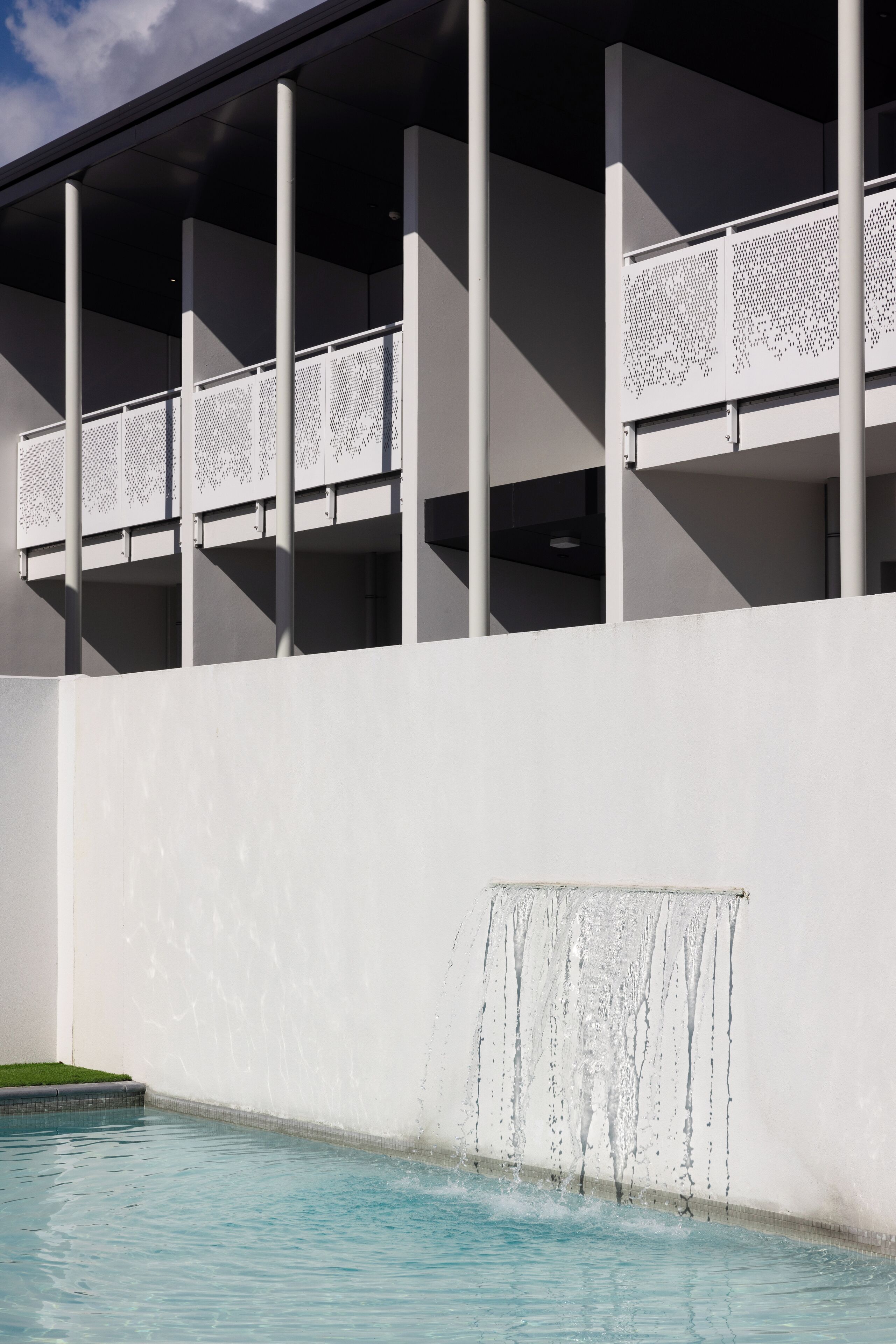 Een modern gebouw met een zwembad, witte muren en een overdekt gedeelte met kolommen.