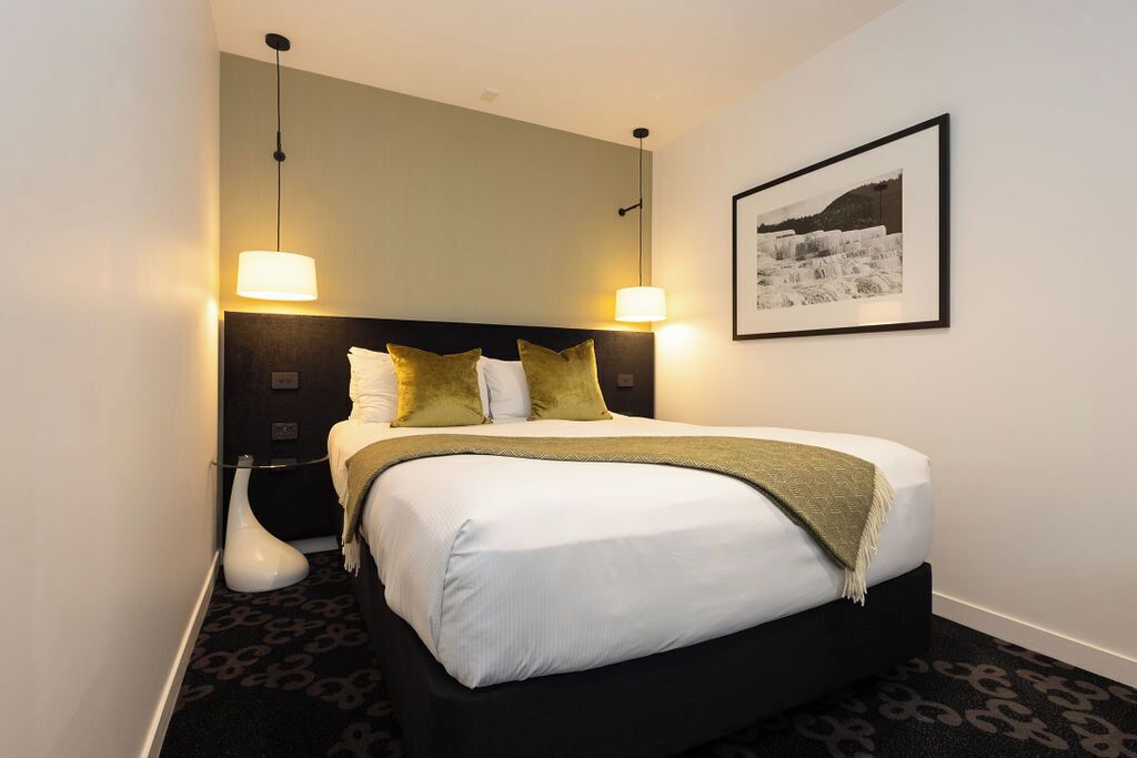 A neatly arranged hotel room with a large bed, two bedside lamps, a framed picture on the wall, and a modern floor lamp.