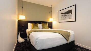 A neatly arranged hotel room with a large bed, two bedside lamps, a framed picture on the wall, and a modern floor lamp.