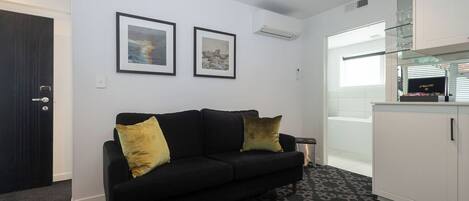 Ein modernes Wohnzimmer mit einer schwarzen Couch, zwei gerahmten Bildern an der Wand, einem Glasvitrine und einem gemusterten Teppich.