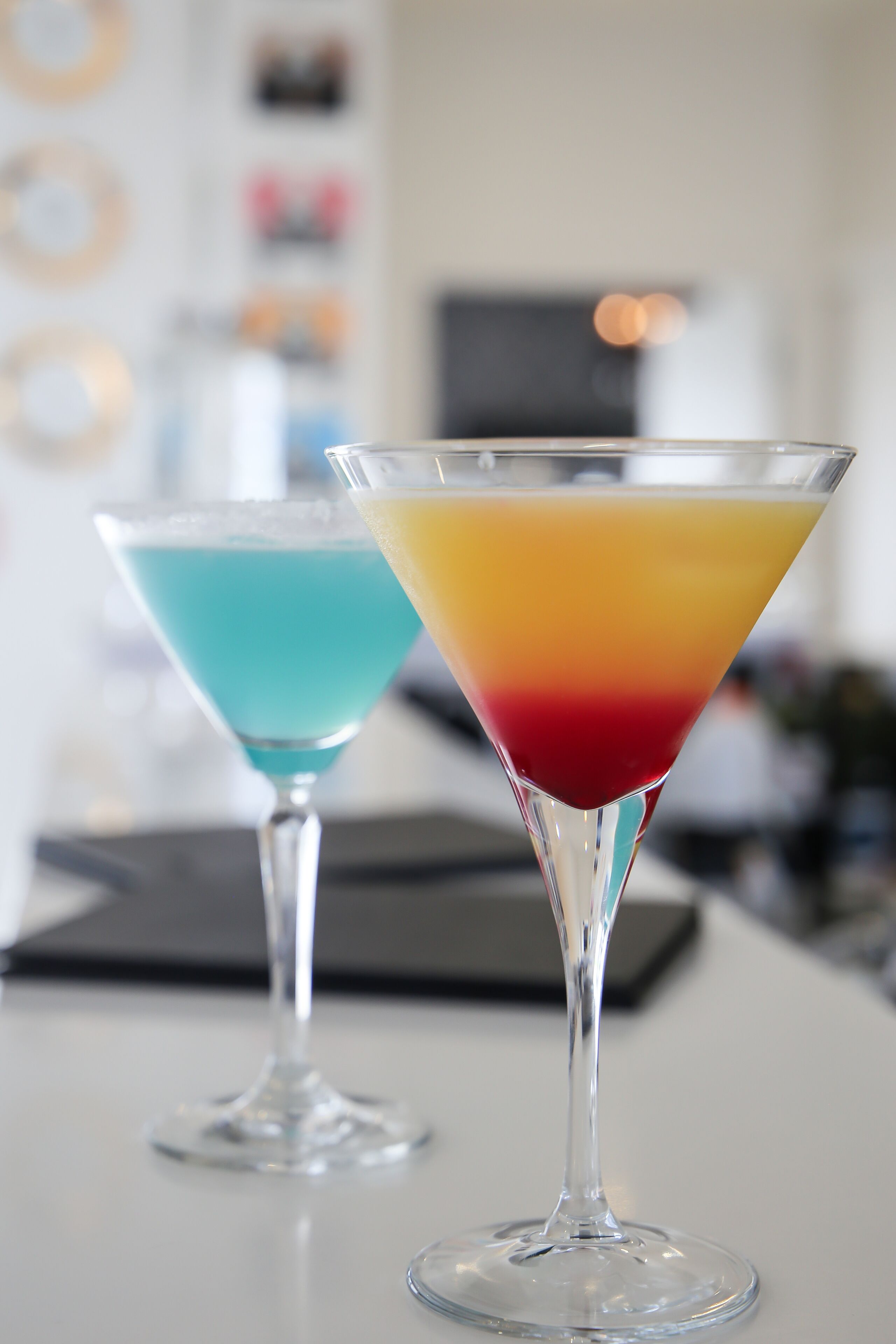 Two martini glasses with layered drinks on a bar counter.