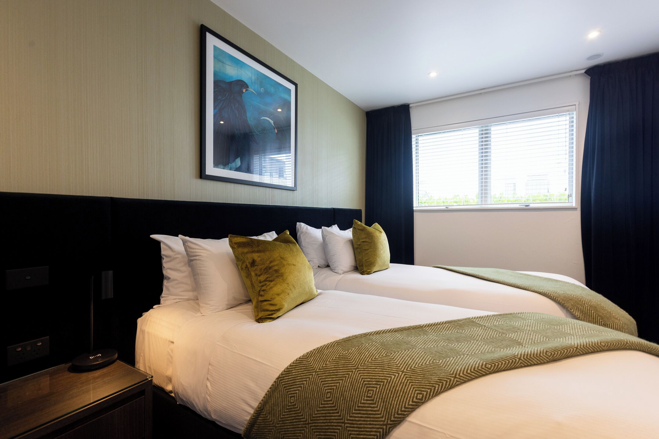 A hotel room with a large bed, a nightstand, a lamp, and a painting on the wall.